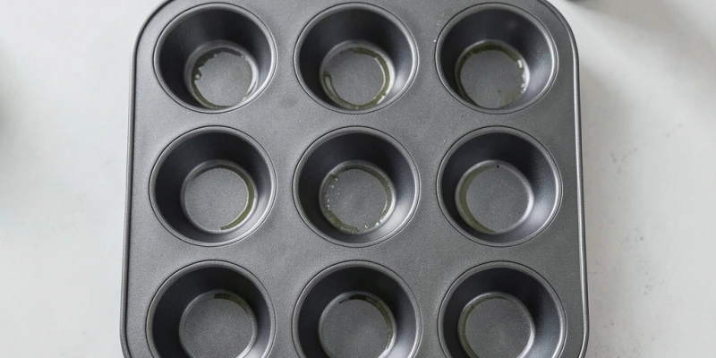 Muffinform von oben, gleichmäßig eingesprüht – man sieht den feinen Ölfilm auf jeder Mulde, keine Pfützen, kein trockener Fleck
